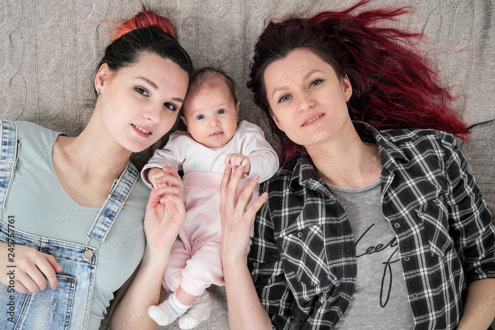 Two young women, a lesbian homosexual couple, are lying on a blanket with a child. Same-sex marriage, adoption. Two young women, a lesbian homosexual couple, are lying on a blanket with a child. Same-sex marriage, adoption.