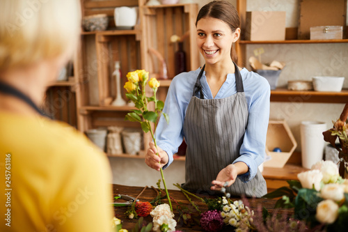 Waist up portrait of smiling young woman selling flowers to client while working in flower shop, copy space photo