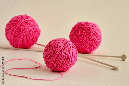 Balls of pink yarn and knitting needles on white background.