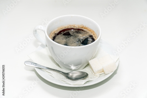 Cup of black coffee on a saucer with a napkin, a teaspoon and lumps of sugar