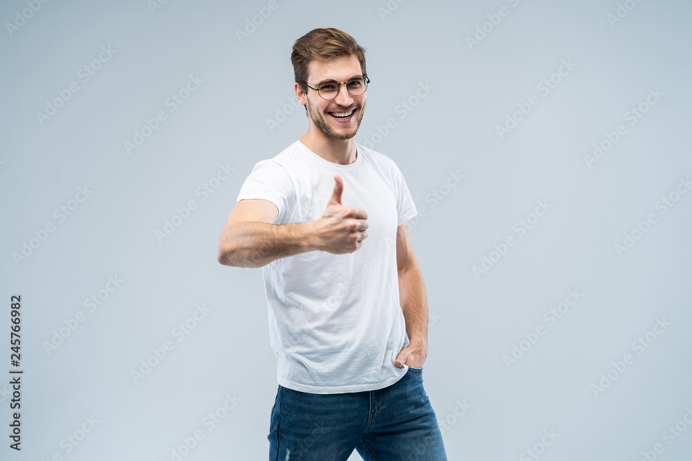 Image of attractive man showing thumb up on camera with happy smile isolated over gray background. Image of attractive man showing thumb up on camera with happy smile isolated over gray background.