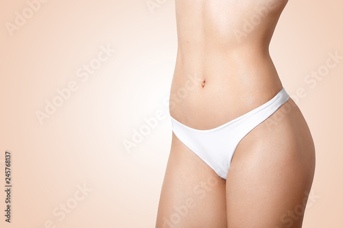Cropped image of unrecognizaable slim woman with perfect body shape, has motivation for sport and healthy lifestyle, demonstrates good figure, wears white panties, isolated over beige background