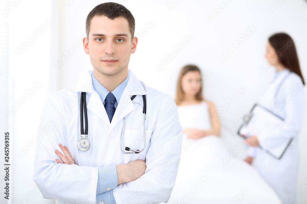 Medicine doctor standing and smiling on the background with patient in the bed Medicine doctor standing and smiling on the background with patient in the bed