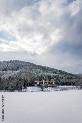 Solitary building in beautiful snowy winter forest landscape, frozen Brezova dam, Shining movie style