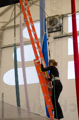 An adult female trapeze artist climbs a ladder leading up to a trapeze platform to perform a jump