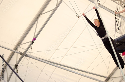 An adult female hangs on a flying trapeze at an indoor gym. The woman is an amateur trapeze artist. photo