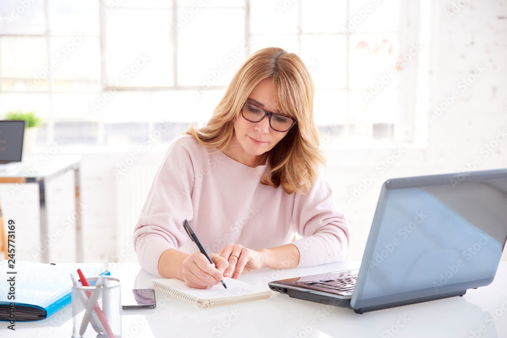 Middle aged businesswoman sitting at office desk and working on business plan Middle aged businesswoman sitting at office desk and working on business plan