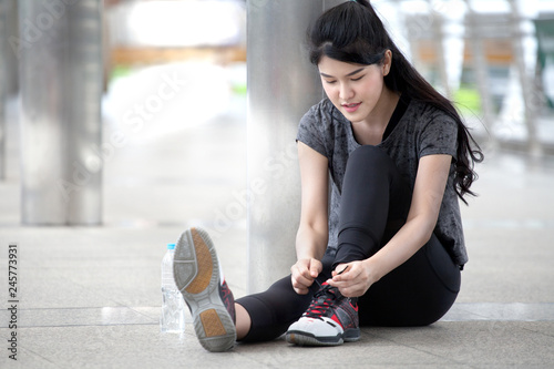 asian fitness young woman runner tying shoelaces before running workout exercising with a water bottle on street in urban city . female athlete sitting on floor