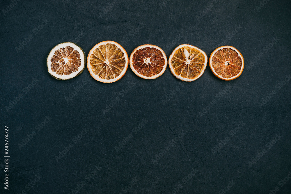 Slices of dried orange orranged in a line on a black background.