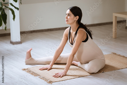 Pregnant woman stretching and training at home. Expectant female makes yoga exercise, healthy pregnancy concept