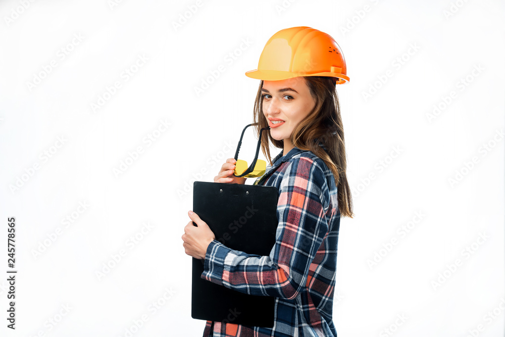 Portrait of beautiful worker model with hard hat and yellow glasses touching her lips isolated on white background. Female builder in helmet holding black folder Portrait of beautiful worker model with hard hat and yellow glasses touching her lips isolated on white background. Female builder in helmet holding black folder