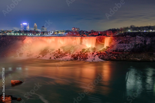 Scenic view of American falls and Bridal Veil Falls illuminated by orange nighttime illumination on Niagara river in Canada. Beautiful depressive winter look of two cascades of famous Niagara falls