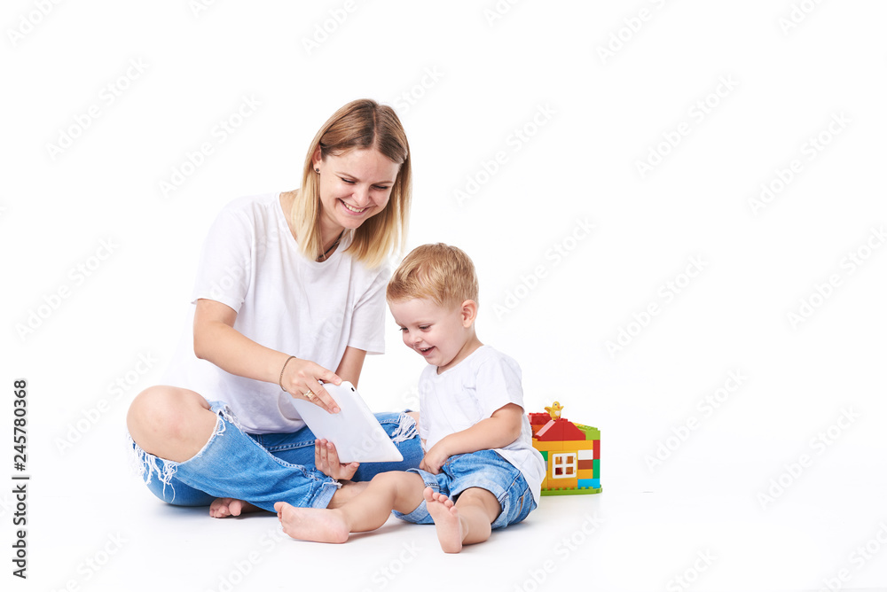 mother and kid play at tablet computer with toys at nursery on white isolated background. Play and fun mother and kid play at tablet computer with toys at nursery on white isolated background. Play and fun