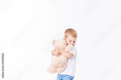 Cute boy plaing with toy fur bear on floor, isolated on white background