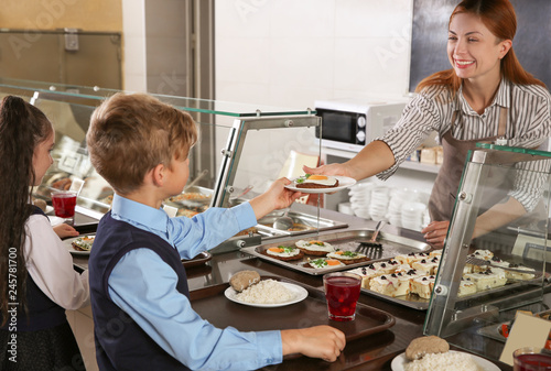 Woman giving plate with healthy food to boy in school canteen photo