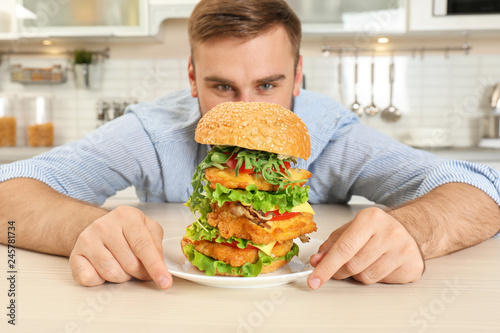 Young hungry man and huge burger in kitchen