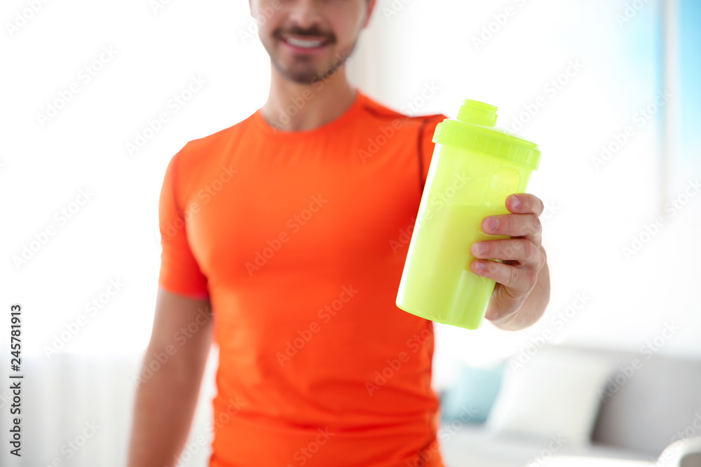 Young sporty man with bottle of protein shake at home, closeup Young sporty man with bottle of protein shake at home, closeup