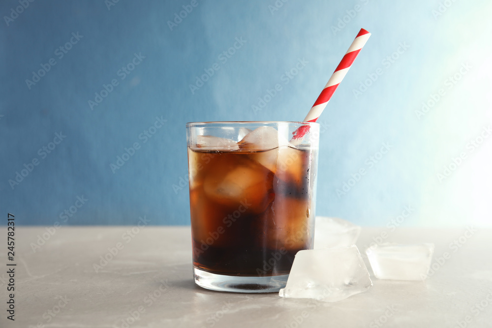 Glass of refreshing cola with ice on table against color background Glass of refreshing cola with ice on table against color background