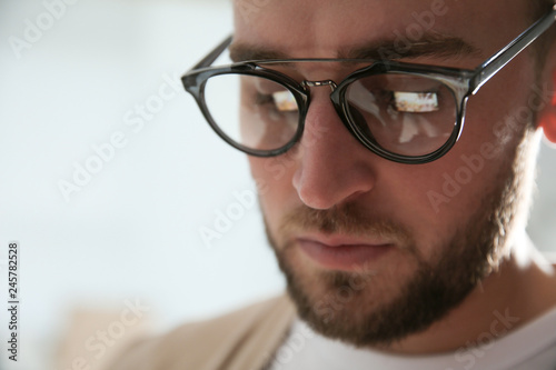 Fototapeta Naklejka Na Ścianę i Meble -  Young man wearing glasses on blurred background, closeup. Ophthalmology service