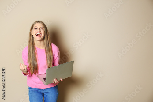 Emotional young woman with laptop celebrating victory on color background. Space for text