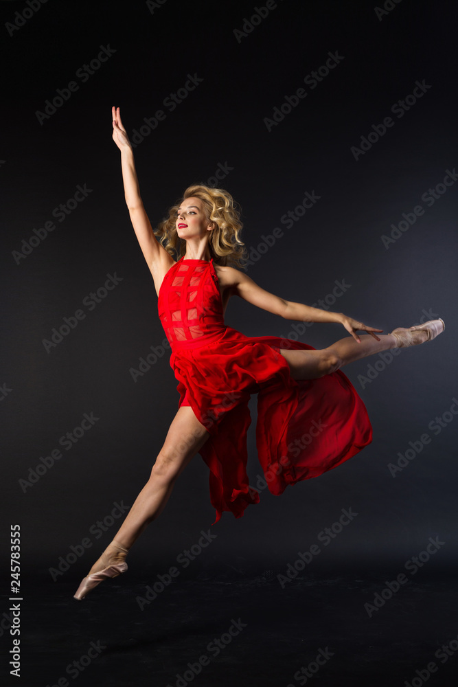 beautiful young girl in red dress jumping in ballet pose on black background