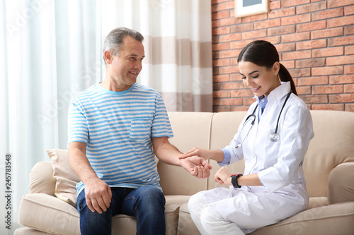 Doctor checking mature man's pulse with fingers at home