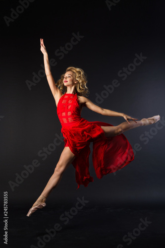 beautiful young girl in red dress jumping in ballet pose on black background