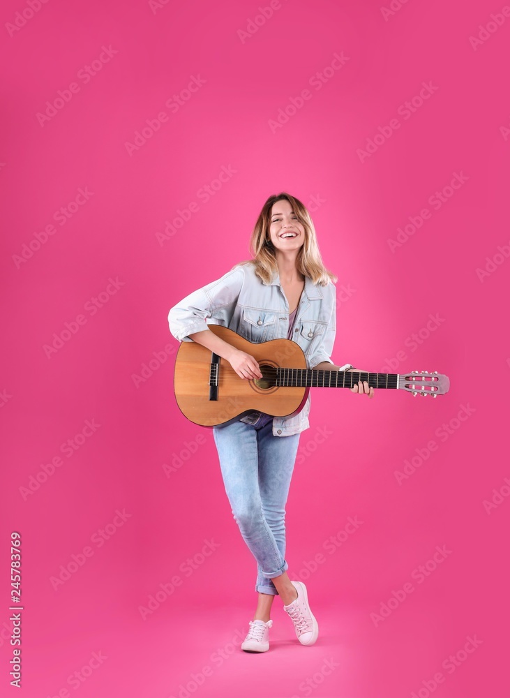 Obraz premium Young woman playing acoustic guitar on color background