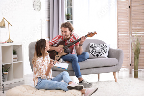 Photography Young man with electric guitar and his girlfriend composing song in living room