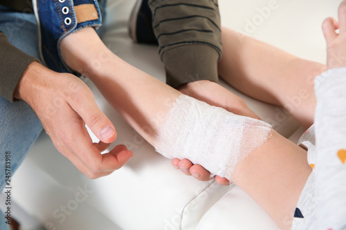 Father applying bandage on daughter's injured knee at home, closeup. First aid