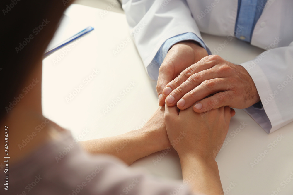 Male doctor comforting woman at table, closeup of hands. Help and support concept