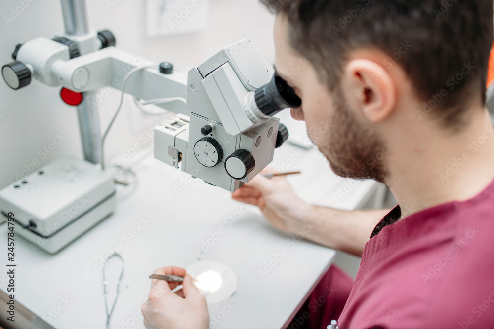 male doctor examines a sample with a microscope at a medical research center. male doctor examines a sample with a microscope at a medical research center.