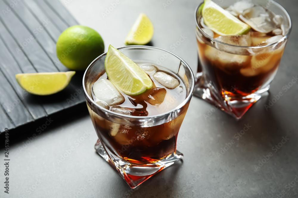 Glasses of cocktail with cola, ice and cut lime on grey background Glasses of cocktail with cola, ice and cut lime on grey background
