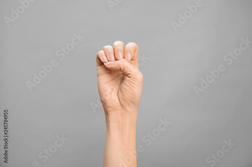 Woman showing E letter on grey background, closeup. Sign language