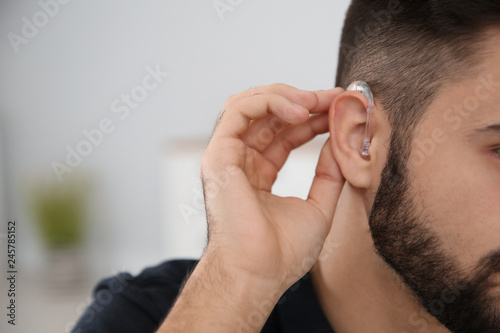 Young man with hearing aid indoors, closeup. Space for text