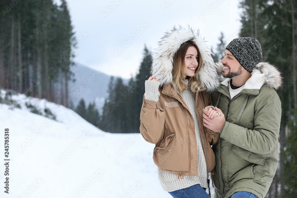 Fototapeta premium Happy couple near conifer forest on snowy day, space for text. Winter vacation