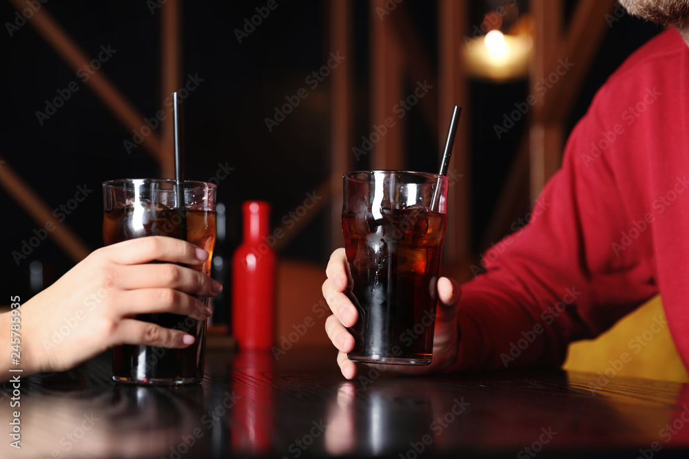 Young couple with glasses of refreshing cola at table indoors, closeup