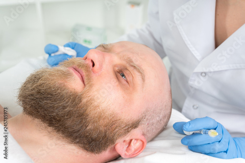 The doctor cosmetologist makes the Rejuvenating facial injections procedure for tightening and smoothing wrinkles on the face skin of a men in a beauty salon.Cosmetology skin care.