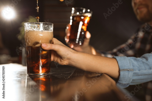 People with cola in glasses at bar counter indoors, closeup. Pouring beverage