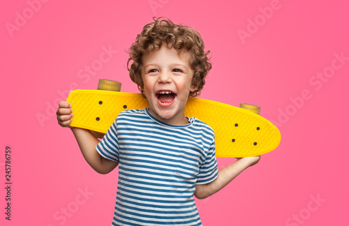 Happy curly boy laughing and holding skateboard