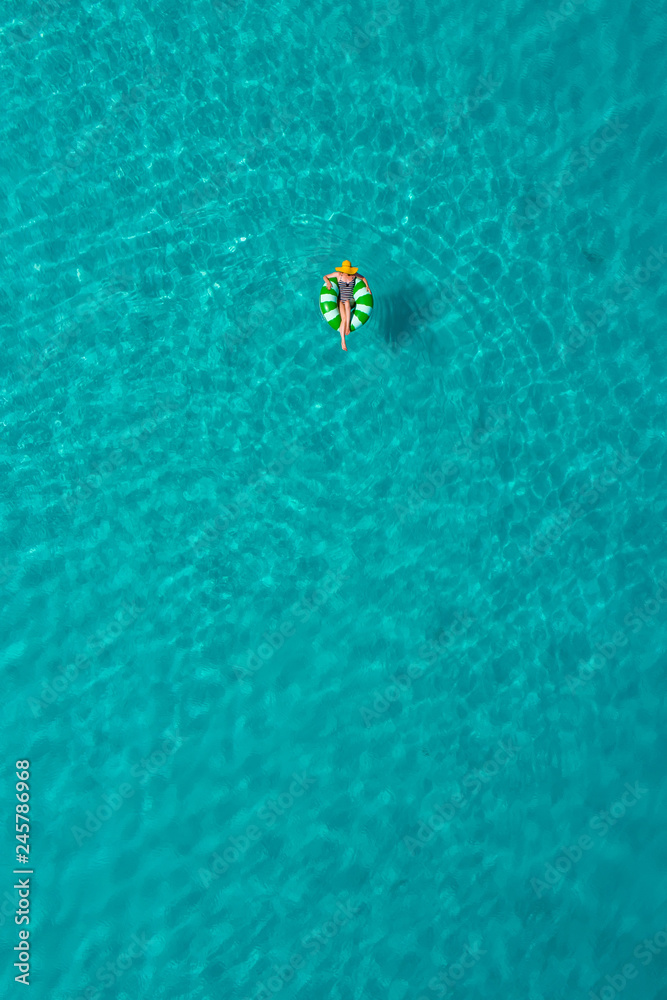 Fototapeta premium Aerial view of slim woman swimming on the swim ring donut in the transparent turquoise sea in Seychelles. Summer seascape with girl, beautiful waves, colorful water. Top view from drone