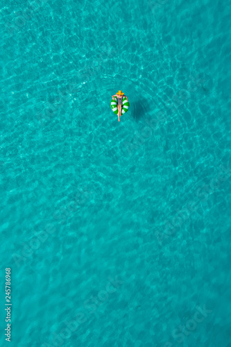 Aerial view of slim woman swimming on the swim ring donut in the transparent turquoise sea in Seychelles. Summer seascape with girl, beautiful waves, colorful water. Top view from drone