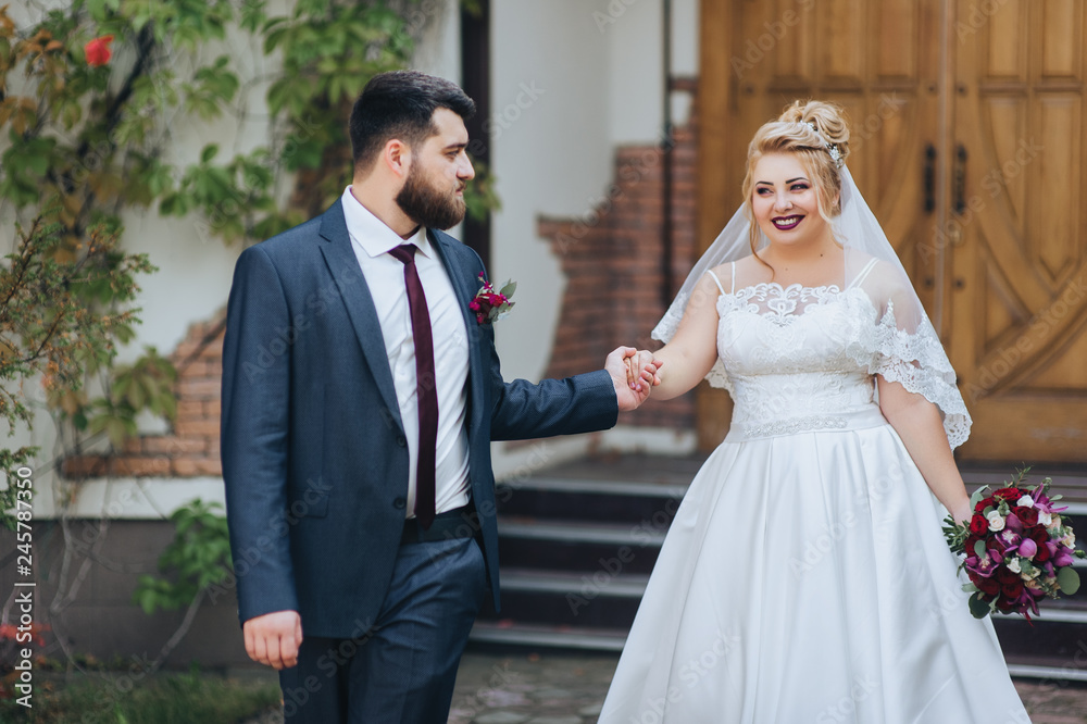 Stylish bearded groom and beautiful blonde bride are walking in a park on nature. Portrait of lovers and smiling newlyweds in a green garden. Wedding photography in the hotel. Stylish bearded groom and beautiful blonde bride are walking in a park on nature. Portrait of lovers and smiling newlyweds in a green garden. Wedding photography in the hotel.