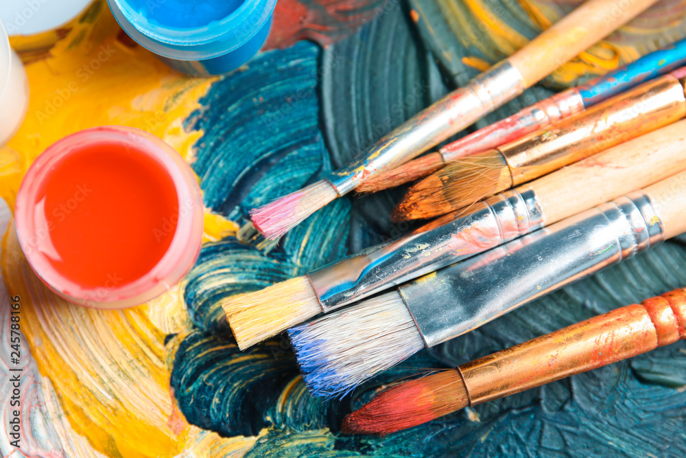 Fototapeta premium Different brushes and jars with paint on palette, top view