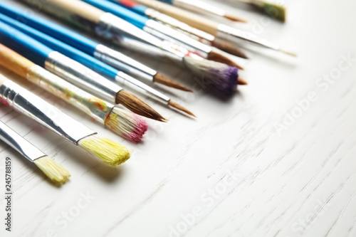 Different paint brushes on wooden table, closeup. Space for text