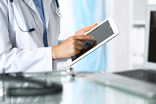 Woman doctor using tablet computer while sitting. Reflecting glass table is a working place of physician. Healthcare  insurance and medicine concept