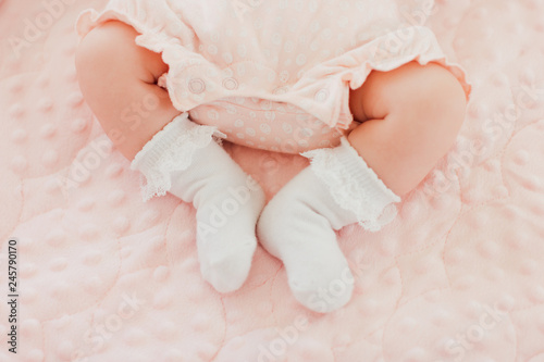 Baby feet in white socks, baby lying on bed, baby's legs, pink background. Newborn, girl