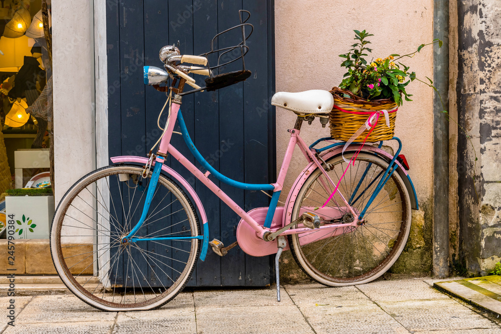 Pink bicycle with flowers near the wall in the beautiful island of Ortigia in Sicily, Italy