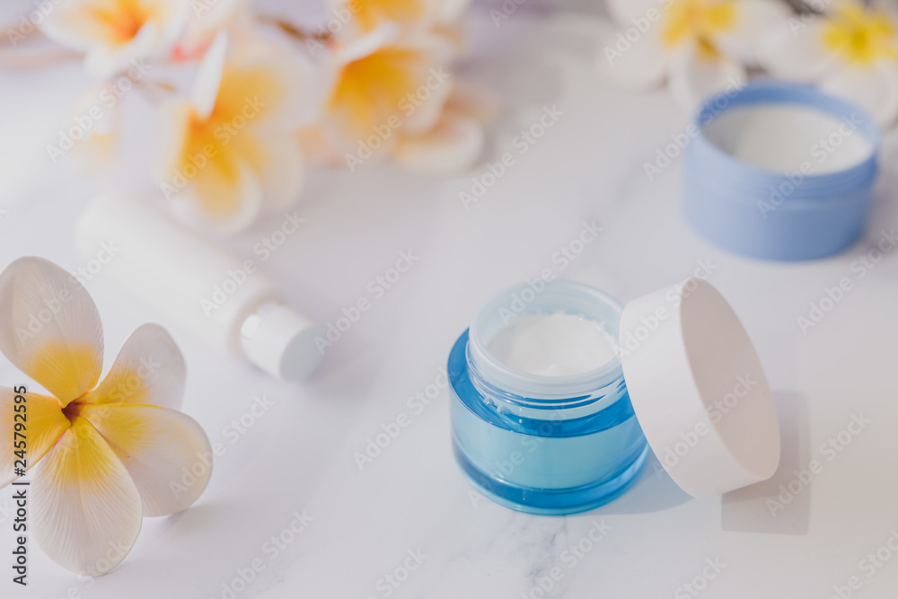 group of skincare products including moisturiser scrub and hand cream pots on marble table with exotic frangipani flowers group of skincare products including moisturiser scrub and hand cream pots on marble table with exotic frangipani flowers