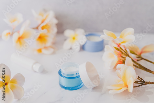 group of skincare products including moisturiser scrub and hand cream pots on marble table with exotic frangipani flowers